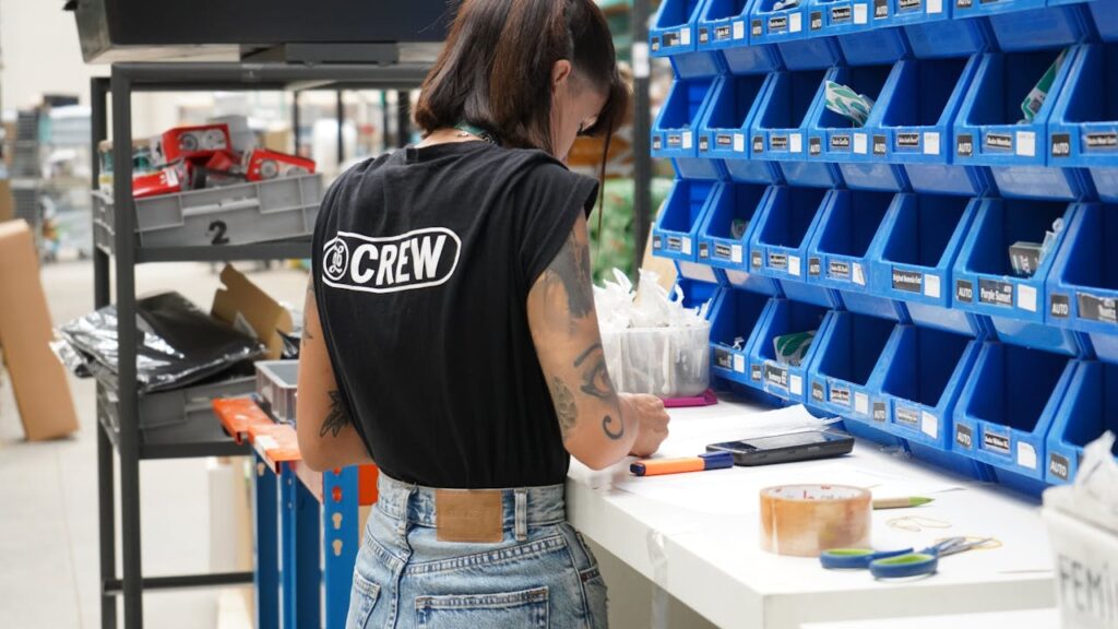 A warehouse worker organizing parts in a storage facility with blue bins and a clipboard.