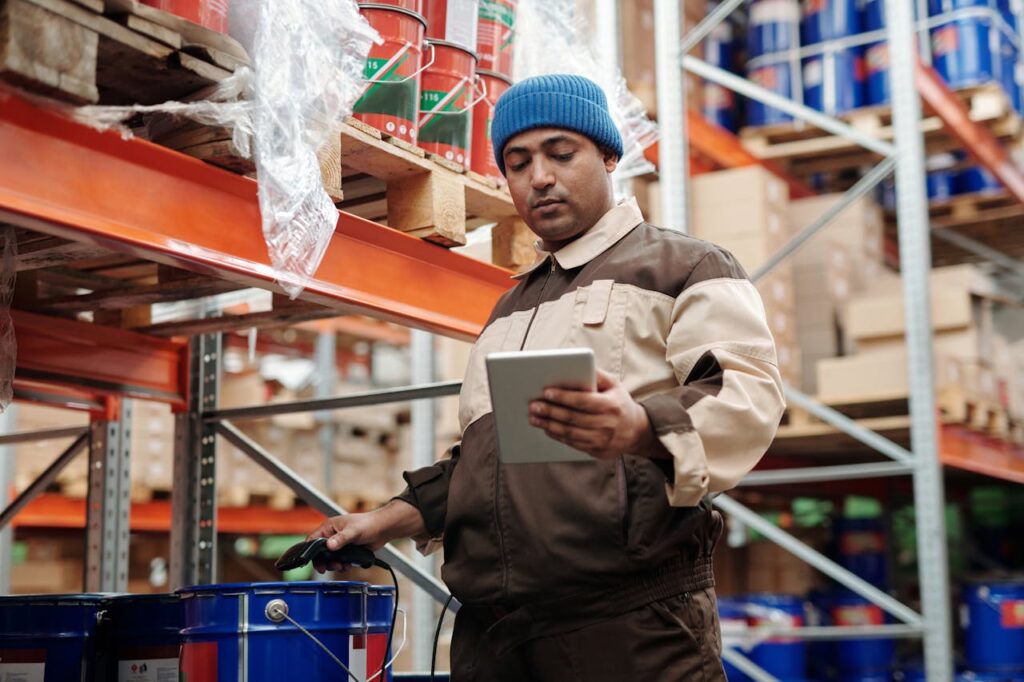 Man in blue beanie uses tablet in a warehouse for inventory management.